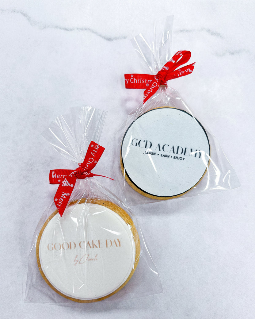 Two round biscuits in clear packaging with red Christmas ribbons on a white marble background