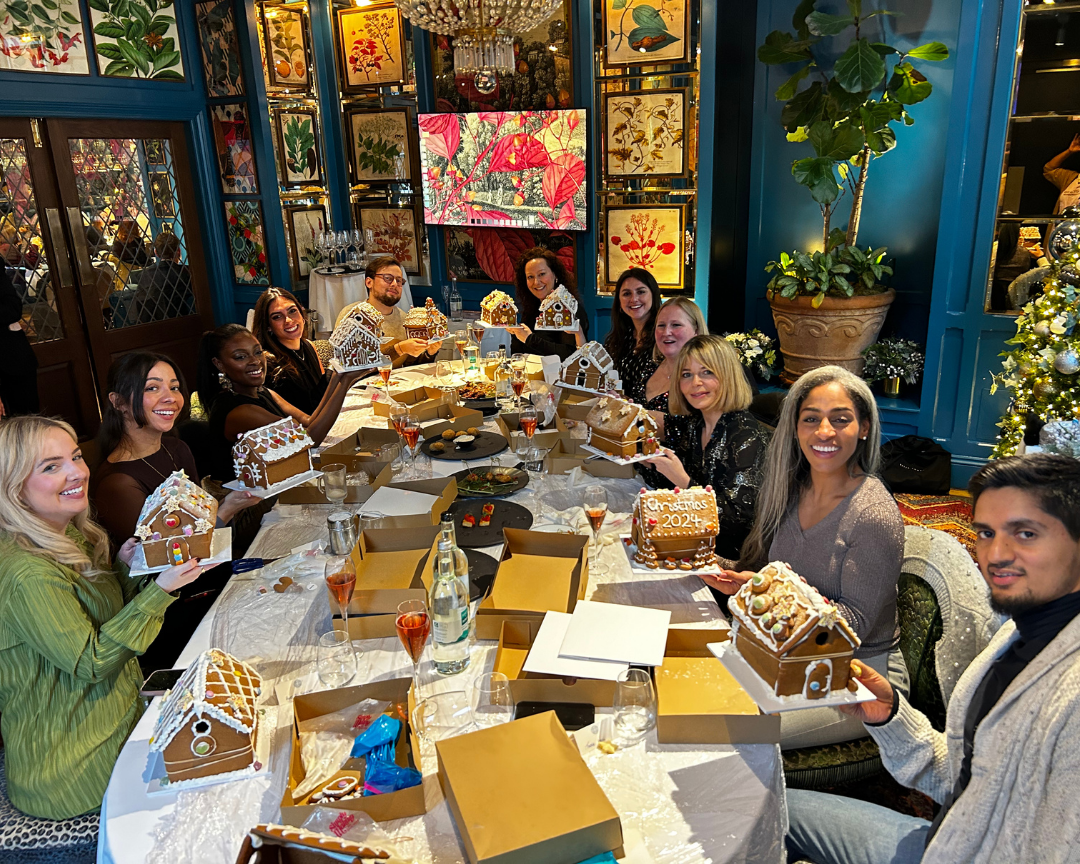 Teams smiling and holding decorated gingerbread houses at a Good Cake Day festive corporate workshop London