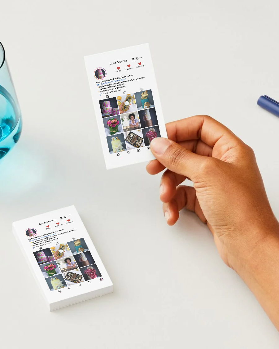 Hand holding a small Instagram-style business card with social media interface design on a light surface.