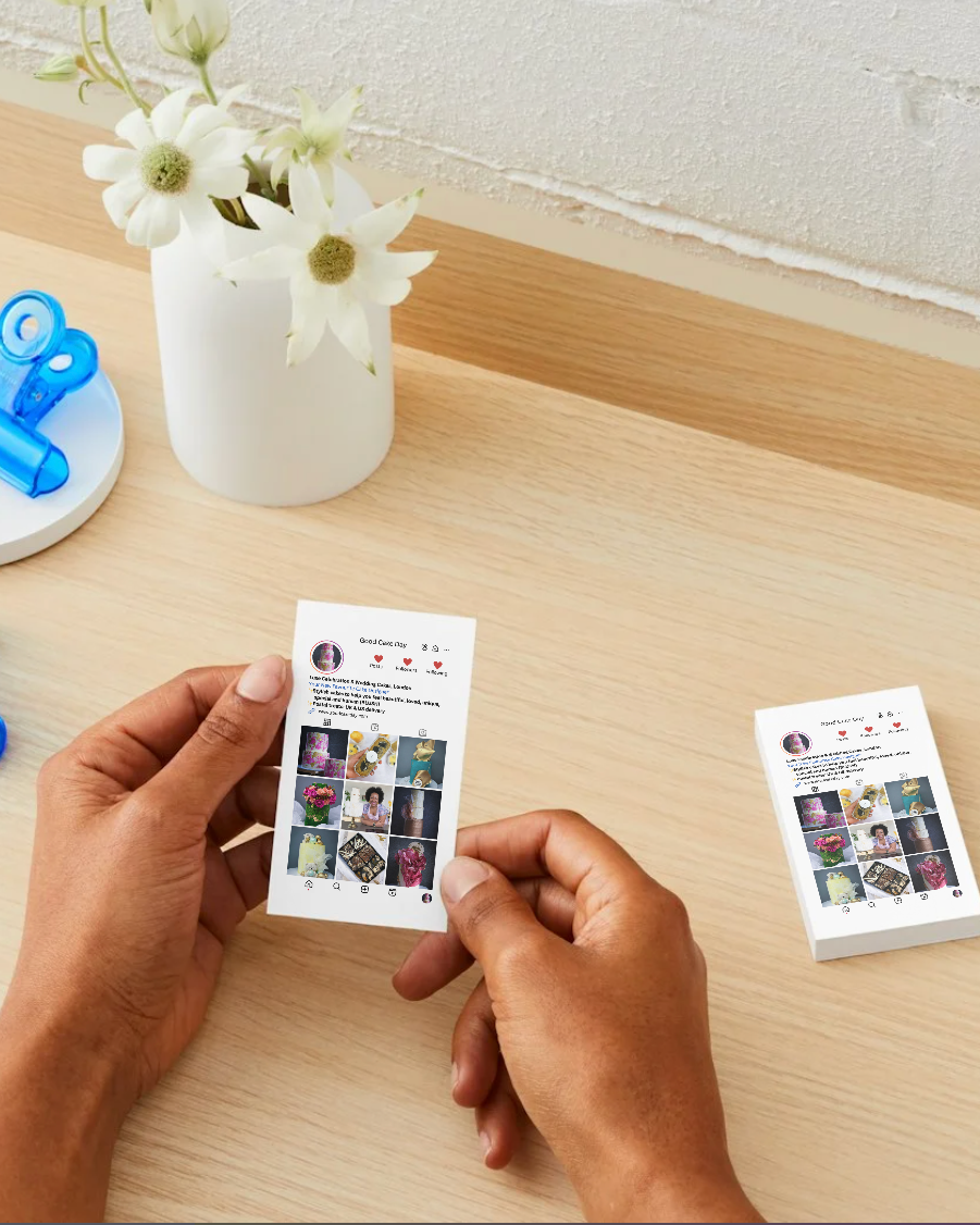 Hands holding an Instagram-style business card  with images on a wooden surface with flowers in the background