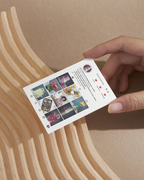 Hand holding an Instagram-style business card with images and text on a wooden surface