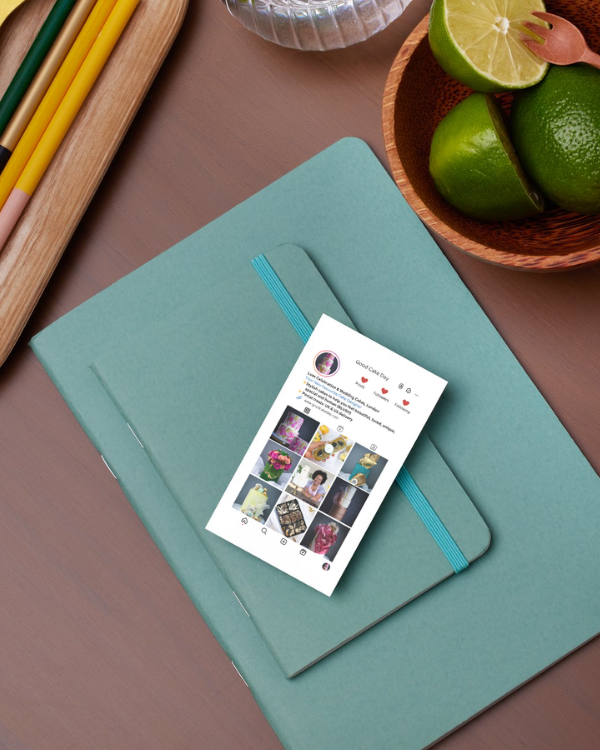 Teal notebook with an Instagram-style business card on top, surrounded by pencils and limes on a brown surface