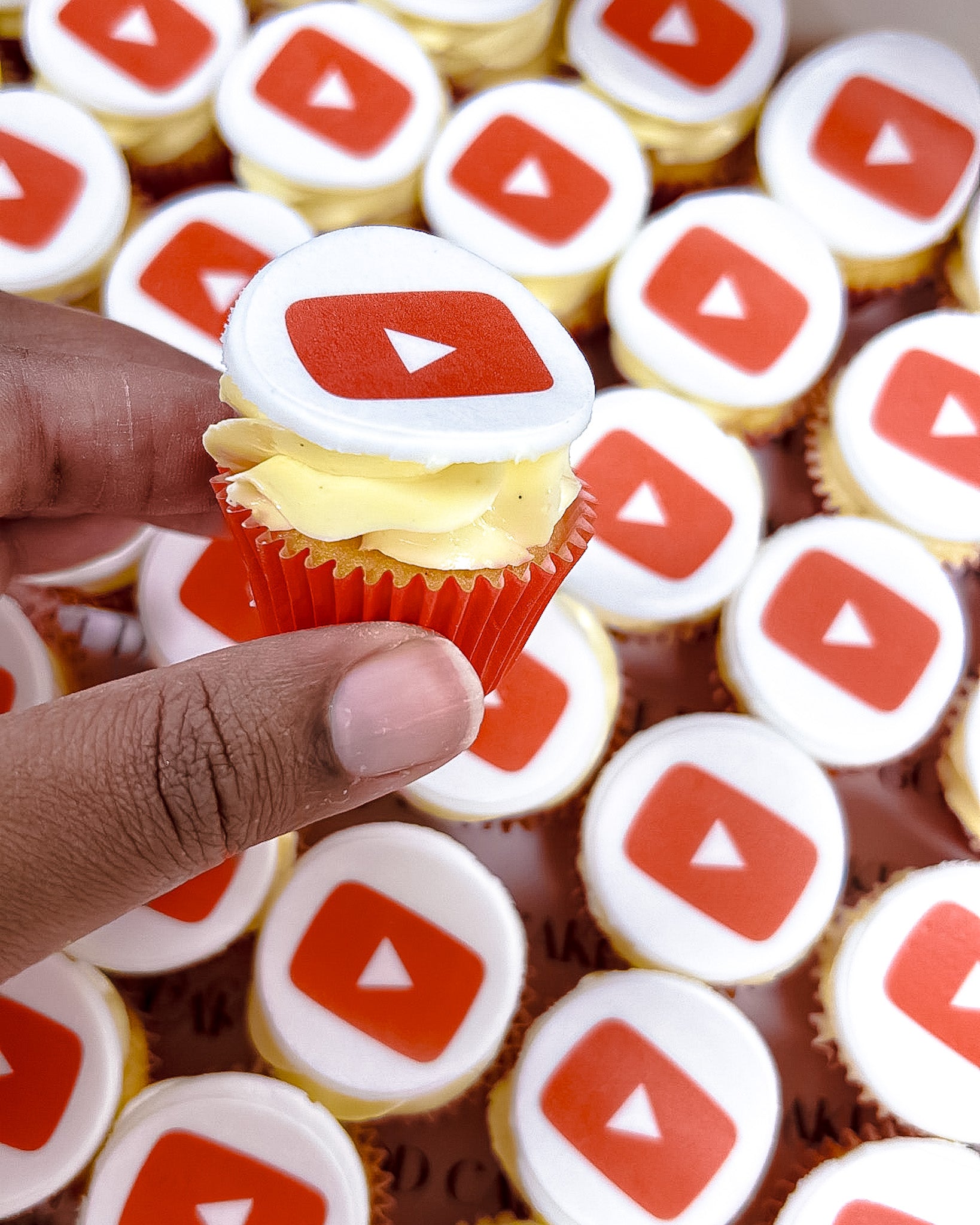 Mini Cupcake with YouTube logo held by a hand, surrounded by more cupcakes with similar designs.