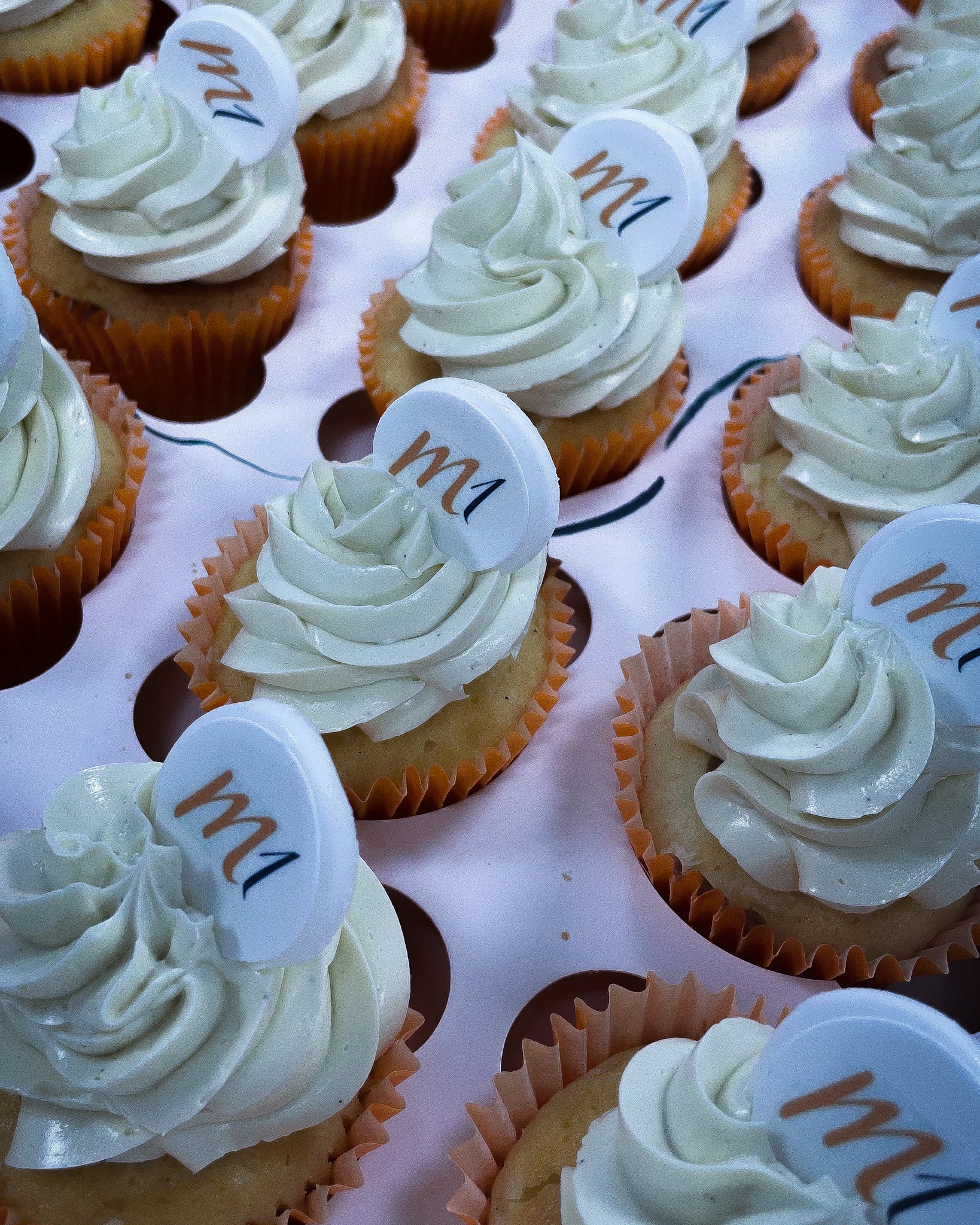 Cupcakes with white frosting and visible 'm1 logo on a pink tray.