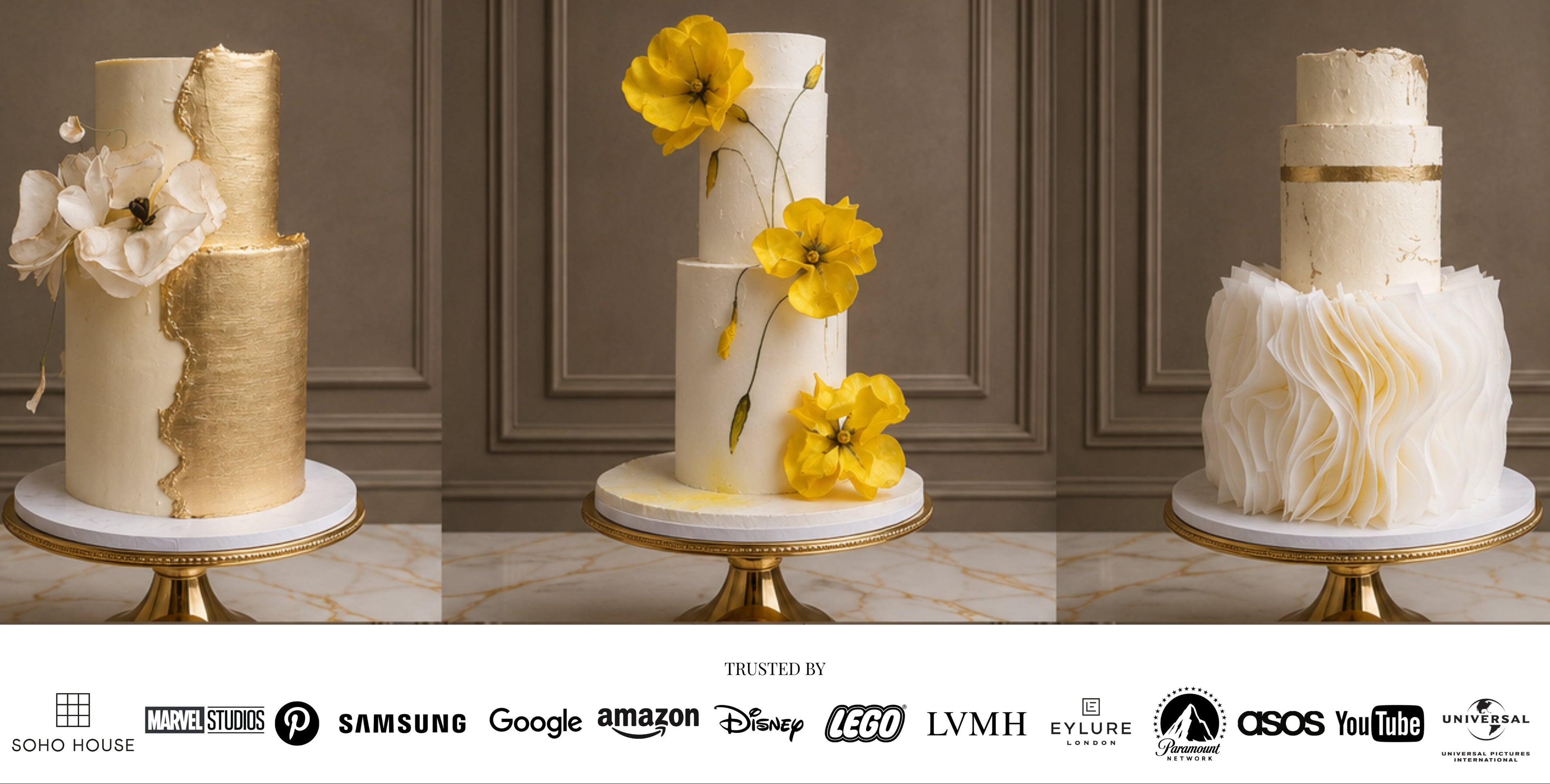 Three elegant white and gold tiered cakes displayed on gold pedestal stands against a dark paneled wall, with a row of sponsor logos along the bottom.