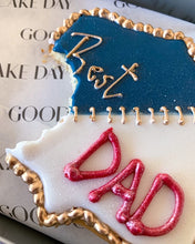 Load image into Gallery viewer, Large blue and white cookie with gold trimmings with the word Best written in gold at the top left hand corner and the word Dad written in red at the bottom right corner. A bite has been taken off the bottom left corner of the cookie and there golden stitches connecting the blue and white sides of the cookie. 
