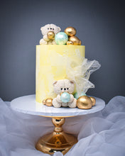 Load image into Gallery viewer, yellow and white warercolour cake with white teddies on top and in front of the cake with a selection of pistachio mint and gold balls at the bottom and top of the cake
